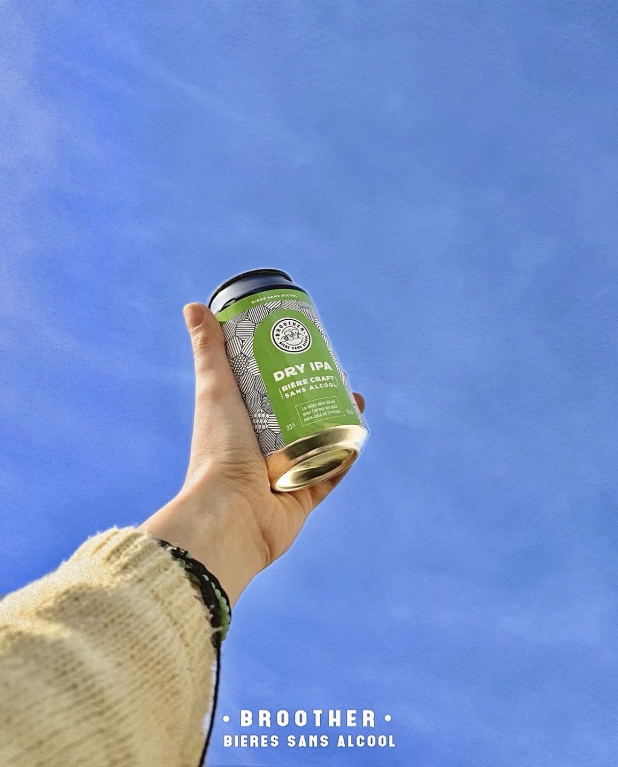 Une main tient une canette de bière sans alcool BROOTHER dans une ambiance de bar